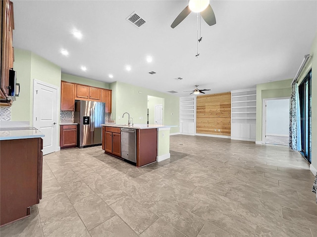 kitchen with ceiling fan, light tile patterned floors, backsplash, an island with sink, and stainless steel appliances