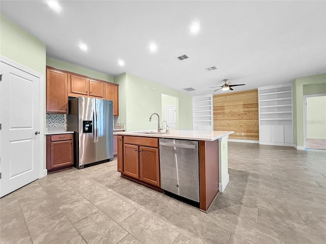 kitchen featuring brown cabinets, a center island with sink, light countertops, appliances with stainless steel finishes, and a sink