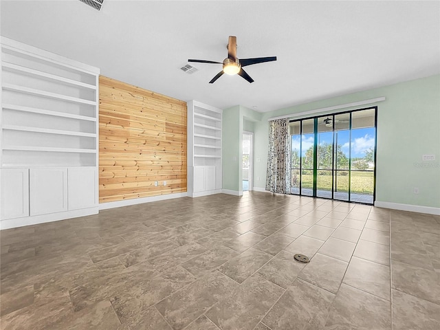 spare room with wooden walls, visible vents, built in features, baseboards, and ceiling fan