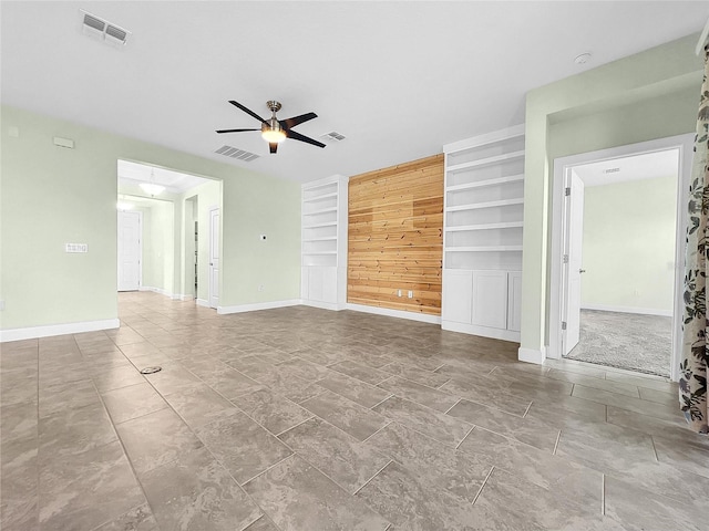 unfurnished living room with built in shelves, visible vents, baseboards, and a ceiling fan