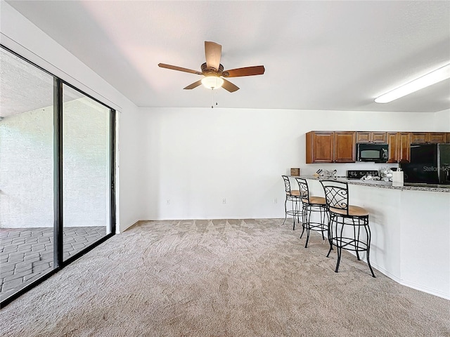 kitchen featuring light carpet, a kitchen breakfast bar, ceiling fan, and black appliances