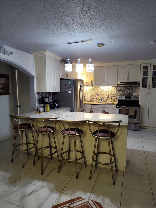 kitchen with kitchen peninsula, appliances with stainless steel finishes, a breakfast bar, a textured ceiling, and white cabinetry