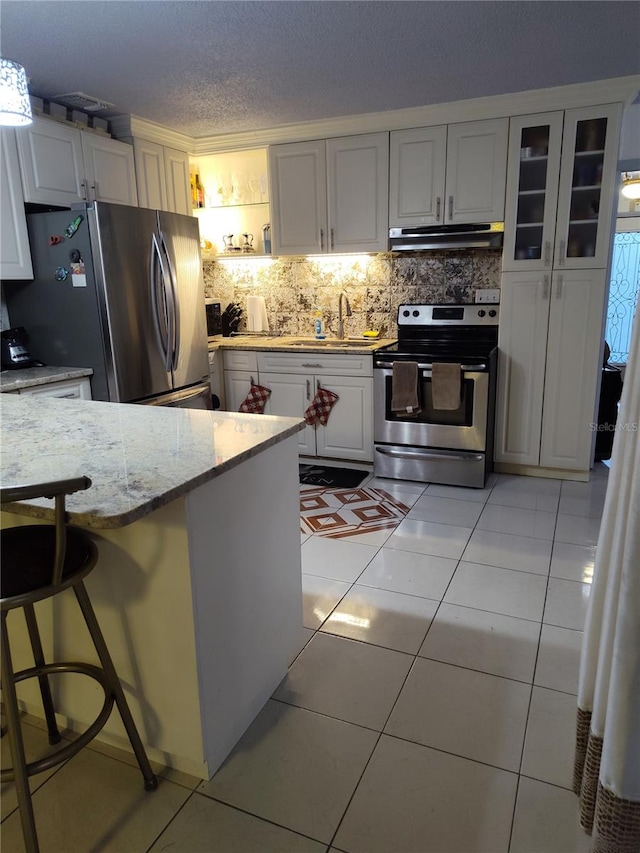 kitchen with a kitchen breakfast bar, light tile patterned flooring, light stone counters, white cabinetry, and stainless steel appliances