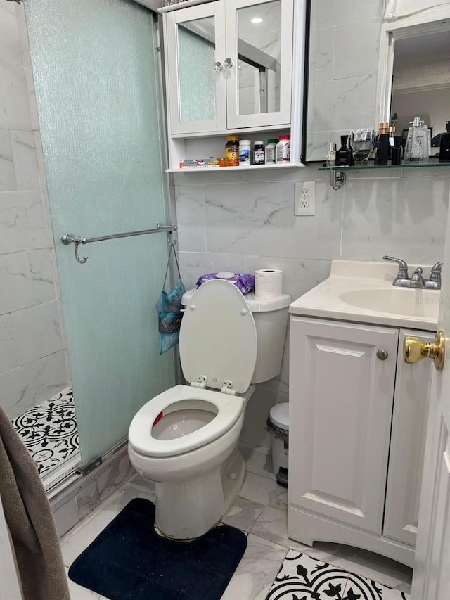 bathroom with vanity, a shower with shower door, tile walls, and toilet