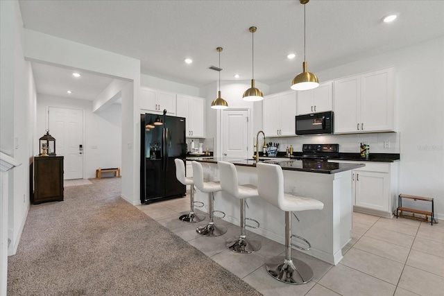 kitchen featuring light tile floors, white cabinetry, decorative light fixtures, black appliances, and a center island with sink