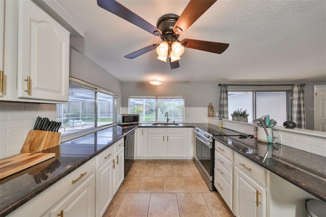 kitchen with appliances with stainless steel finishes, dark stone counters, sink, light tile patterned flooring, and ceiling fan