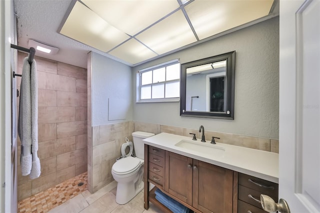 bathroom featuring tile patterned flooring, tile walls, tiled shower, toilet, and vanity