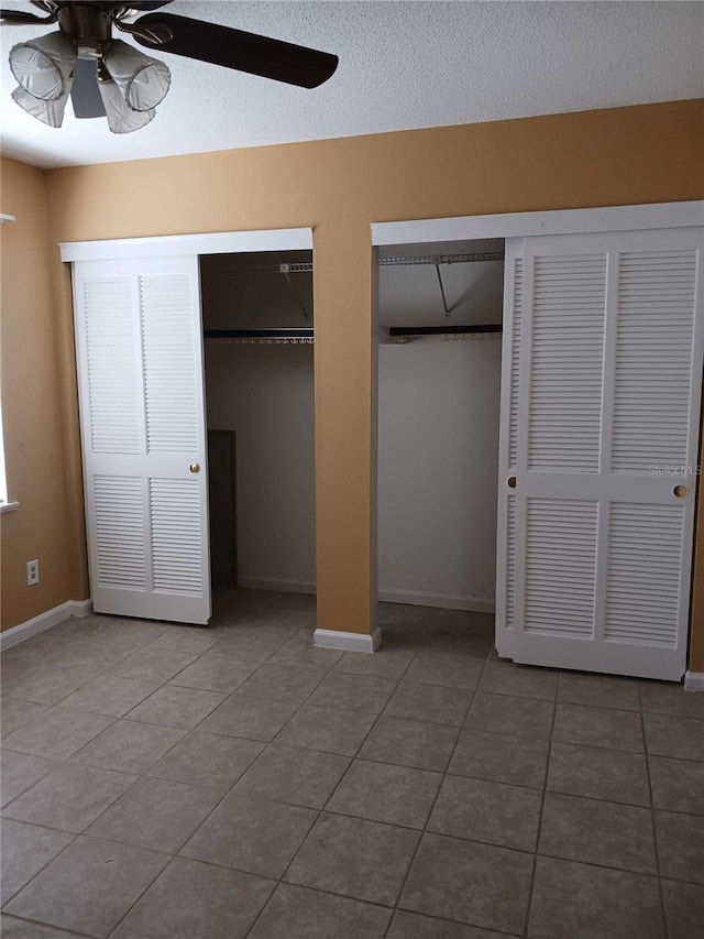 unfurnished bedroom with ceiling fan, tile floors, two closets, and a textured ceiling