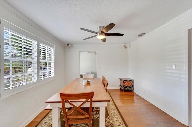 dining space with wood-type flooring, ceiling fan, crown molding, and a textured ceiling