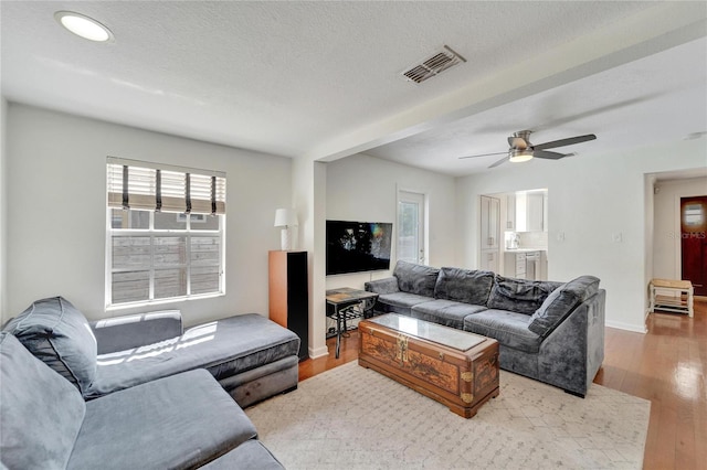 living room with a wealth of natural light, light hardwood / wood-style floors, ceiling fan, and a textured ceiling