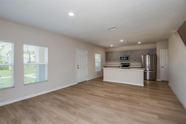 kitchen with gray cabinets, stainless steel appliances, an island with sink, a textured ceiling, and light wood-type flooring