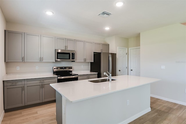 kitchen featuring stainless steel appliances, sink, a center island with sink, and light hardwood / wood-style floors