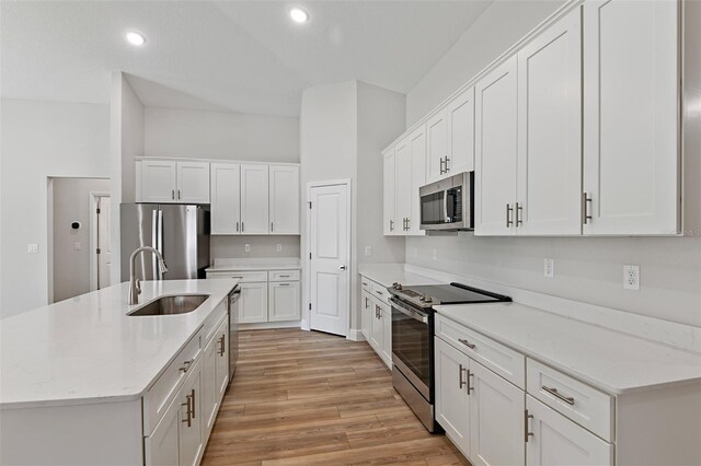 kitchen featuring light wood-type flooring, appliances with stainless steel finishes, white cabinetry, sink, and a center island with sink