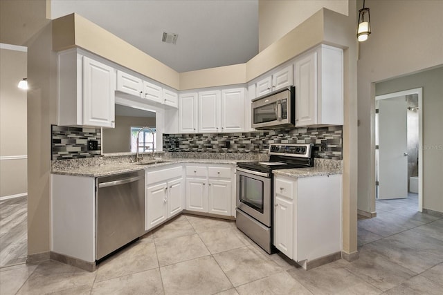 kitchen with backsplash, white cabinetry, stainless steel appliances, and light stone countertops