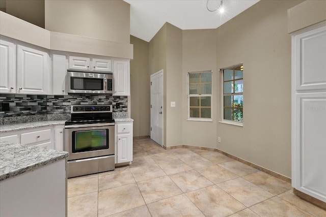 kitchen with light stone countertops, white cabinetry, backsplash, stainless steel appliances, and light tile floors