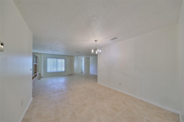 unfurnished room with baseboards, visible vents, a chandelier, and a textured ceiling