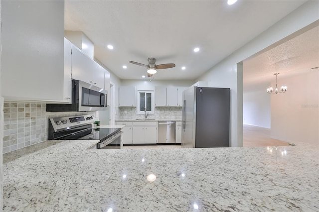 kitchen with sink, appliances with stainless steel finishes, light stone countertops, ceiling fan with notable chandelier, and white cabinets