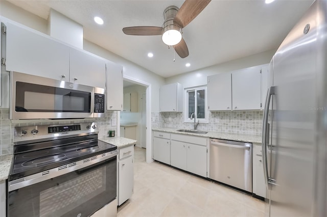 kitchen featuring a sink, white cabinetry, appliances with stainless steel finishes, light stone countertops, and tasteful backsplash