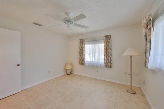 empty room featuring baseboards, visible vents, ceiling fan, a textured ceiling, and light tile patterned flooring