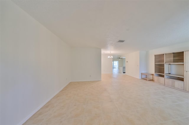 unfurnished living room with light tile patterned floors, baseboards, visible vents, a textured ceiling, and a notable chandelier