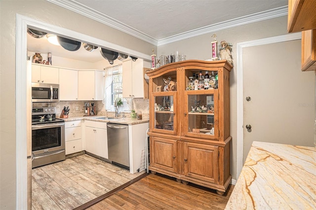 kitchen with light hardwood / wood-style flooring, white cabinetry, backsplash, ornamental molding, and appliances with stainless steel finishes