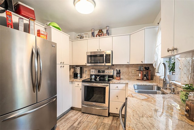 kitchen featuring appliances with stainless steel finishes, backsplash, white cabinetry, sink, and light wood-type flooring