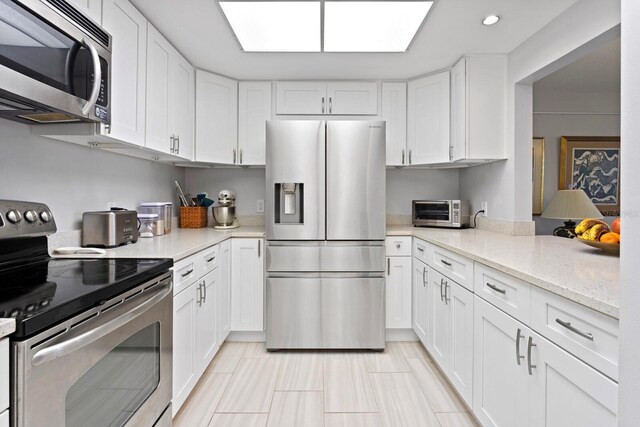 kitchen with white cabinetry, appliances with stainless steel finishes, a skylight, and light stone counters