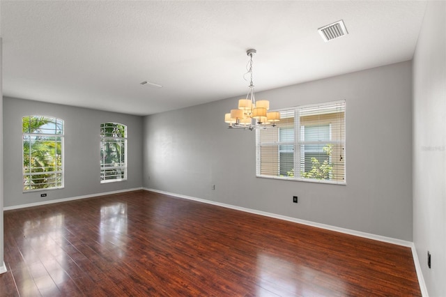 spare room featuring wood-type flooring, a healthy amount of sunlight, and a notable chandelier