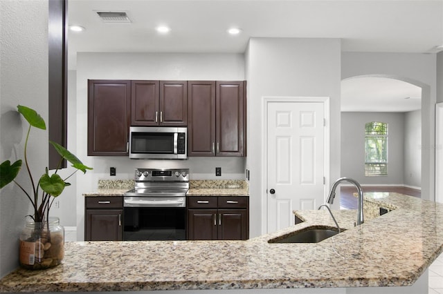 kitchen with dark brown cabinets, sink, stainless steel appliances, and light stone counters