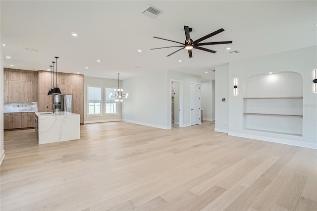 unfurnished living room with ceiling fan with notable chandelier, light hardwood / wood-style flooring, and sink