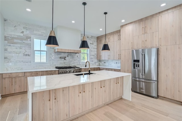 kitchen featuring appliances with stainless steel finishes, sink, a kitchen island with sink, and light hardwood / wood-style flooring