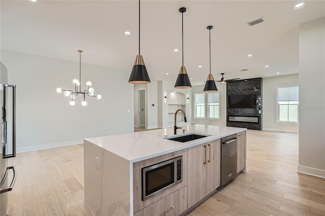 kitchen with stainless steel appliances, a center island with sink, light hardwood / wood-style floors, and decorative light fixtures