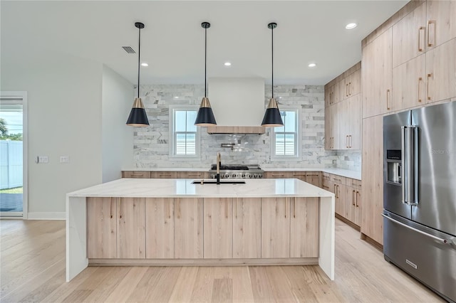 kitchen featuring a wealth of natural light, light hardwood / wood-style flooring, an island with sink, high end fridge, and light brown cabinetry