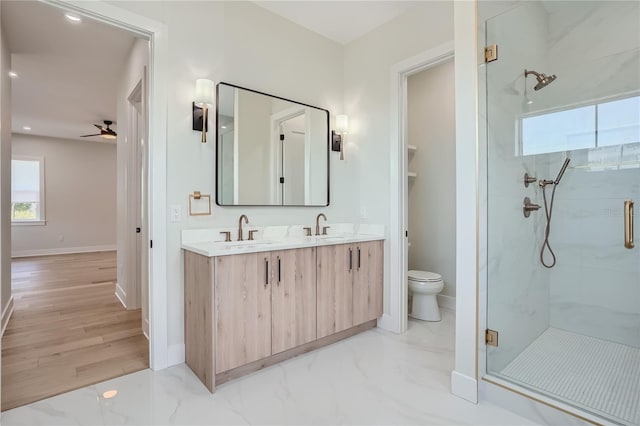 bathroom featuring ceiling fan, a shower with shower door, dual bowl vanity, hardwood / wood-style flooring, and toilet