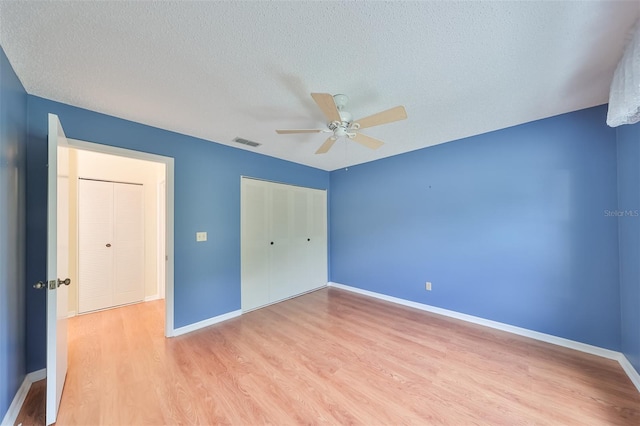 unfurnished bedroom featuring a closet, light hardwood / wood-style floors, ceiling fan, and a textured ceiling