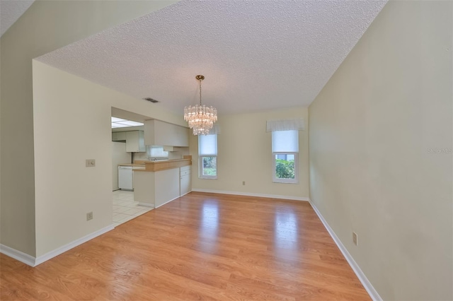 unfurnished living room with a textured ceiling, a notable chandelier, and light wood-type flooring