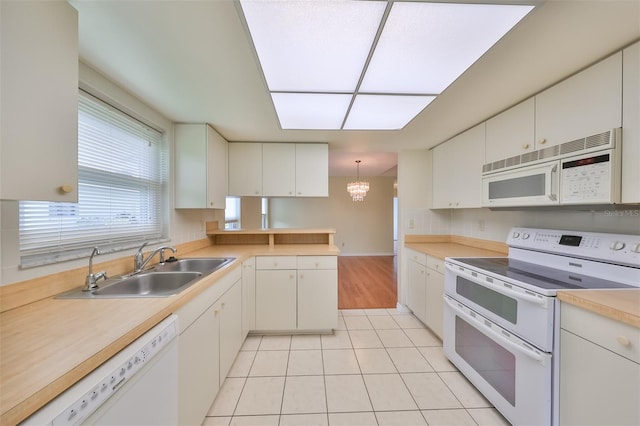 kitchen featuring white cabinets, white appliances, light tile flooring, an inviting chandelier, and sink