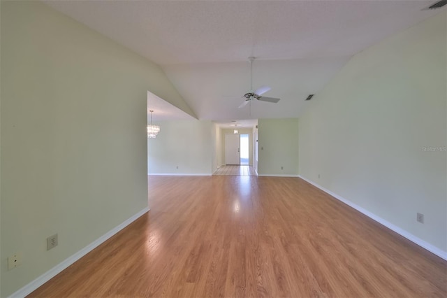 spare room with ceiling fan with notable chandelier, vaulted ceiling, and light wood-type flooring