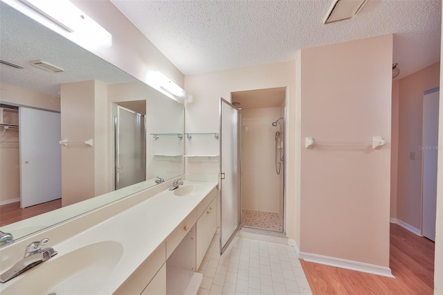 bathroom featuring tile floors, a shower with door, dual bowl vanity, and a textured ceiling