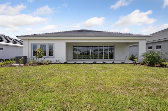 rear view of property with stucco siding, central AC unit, and a yard