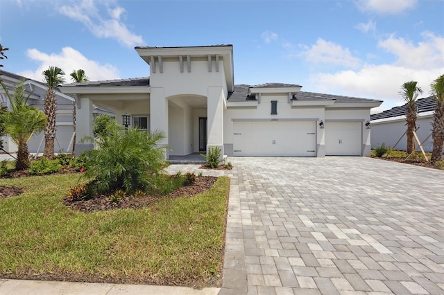 view of front of property with decorative driveway, an attached garage, a front yard, and stucco siding