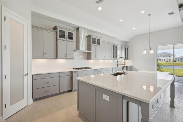 kitchen featuring a sink, visible vents, wall chimney range hood, gray cabinets, and an island with sink