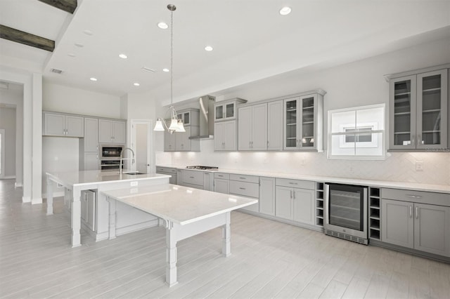 kitchen with wall chimney range hood, light wood-type flooring, tasteful backsplash, beverage cooler, and gray cabinetry