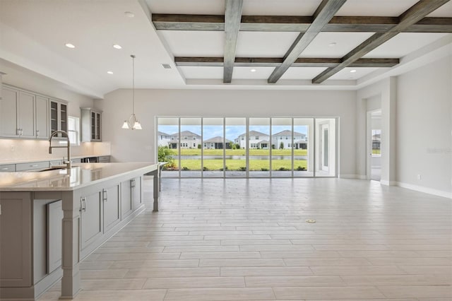 kitchen with light countertops, backsplash, gray cabinetry, open floor plan, and a sink