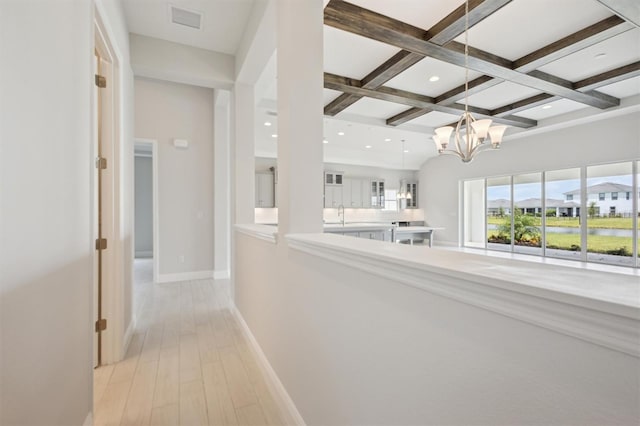 hallway featuring a chandelier, coffered ceiling, sink, beamed ceiling, and light wood-type flooring