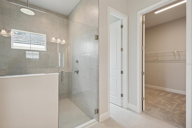 bathroom with a spacious closet, a stall shower, and baseboards