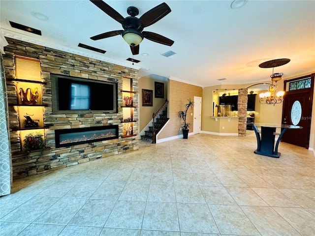 tiled living room with ceiling fan with notable chandelier, a fireplace, and crown molding