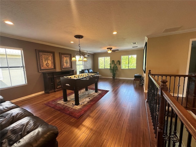 recreation room featuring ornamental molding, dark hardwood / wood-style flooring, ceiling fan with notable chandelier, and a textured ceiling