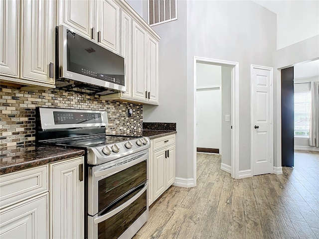 kitchen featuring backsplash, stainless steel appliances, light hardwood / wood-style floors, and dark stone countertops