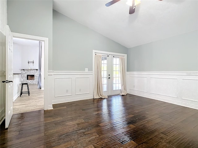 spare room featuring french doors, dark hardwood / wood-style flooring, ceiling fan, high vaulted ceiling, and a fireplace